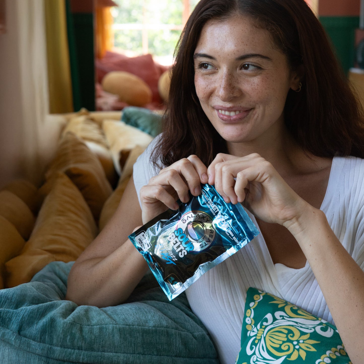 Bluerazz Blast Sour Belts - High Potency 3000MG THC Edibles - Woman Opening Sour Belts Smiling Sitting on Couch - Galaxy Treats in the U.S.
