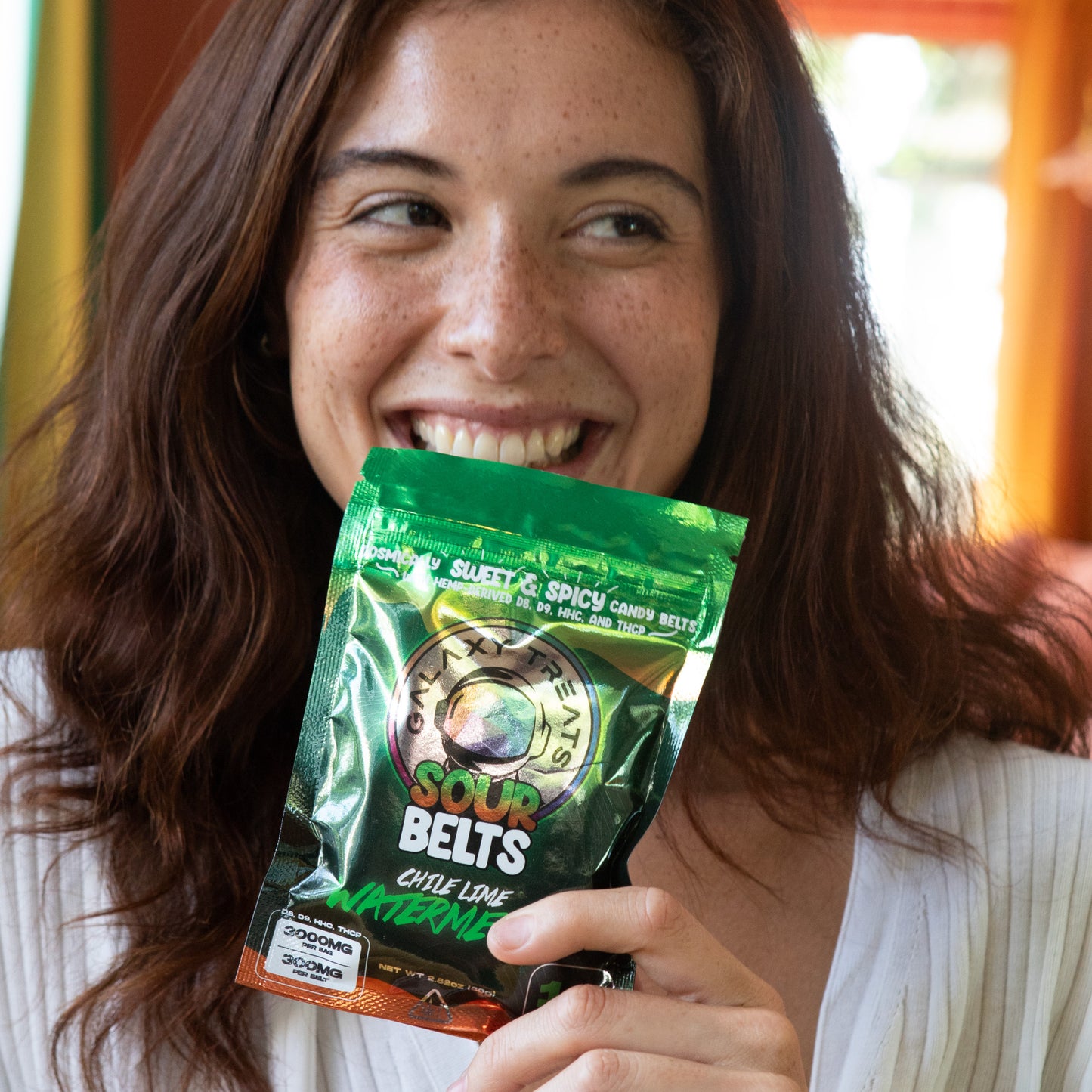 Chile Lime Watermelon Sour Belts - High Potency 300MG THC Edibles - Woman Smiling Holding Packaging in Hand - Galaxy Treats in the U.S.