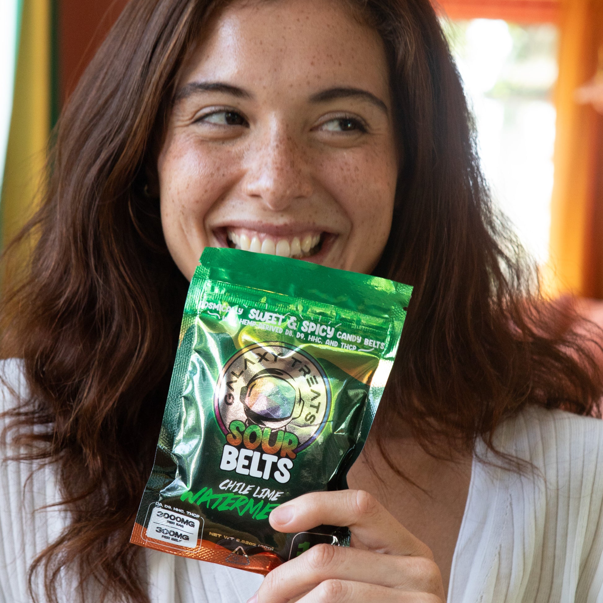Chile Lime Watermelon Sour Belts - High Potency 300MG THC Edibles - Woman Smiling Holding Packaging in Hand - Galaxy Treats in the U.S.